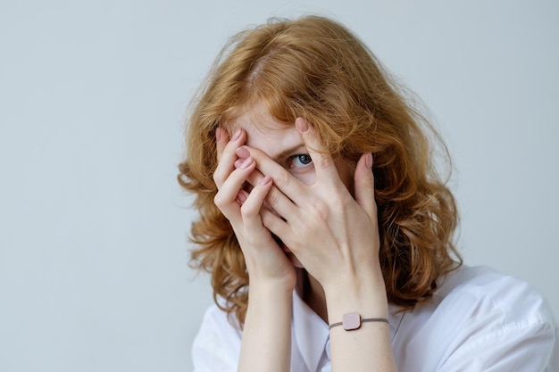 Foto uma garota ruiva com cachos de vergonha cobre o rosto com as mãos e olha por entre os dedos fobia social da geração mais jovem