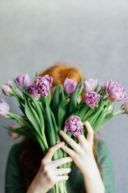 Uma garota ruiva escondeu o rosto atrás de um buquê de tulipas cor de rosa.