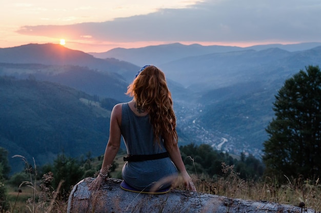 Uma garota se senta à beira do penhasco e olhando para o vale do sol e as montanhas mulher sentada no topo da montanha e contemplando o pôr do sol pôr do sol nos cárpatos ucranianos