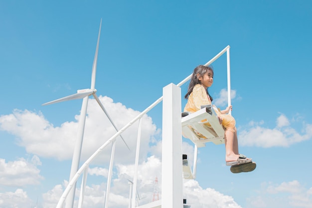 Uma garota se senta em uma cadeira em frente a uma turbina eólica.
