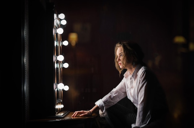 Uma garota se senta na frente de um espelho em um quarto escuro