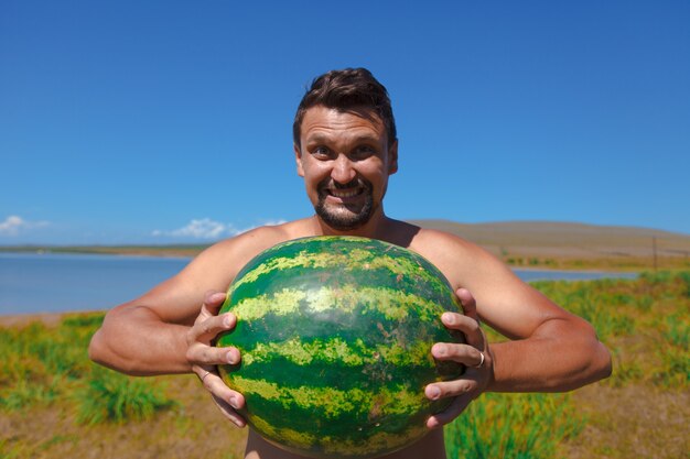 Uma garota se senta na praia e segura uma melancia. amadurecimento de bagas de verão Emoções e humor alegres. Piquenique de verão.