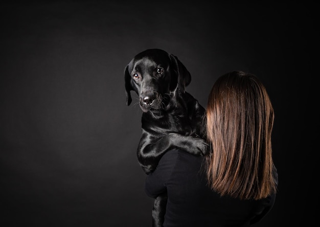 Uma garota segura um cachorro Labrador Retriever em seus braços Capturado em um estúdio fotográfico em um fundo preto