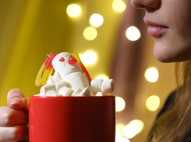 uma garota segura um copo vermelho com um boneco de neve marshmallow nas mãos