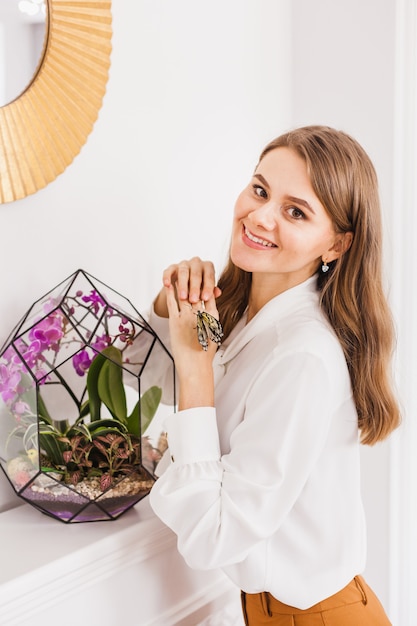 Uma garota segura uma florariumov, forma de vidro com suculentas, pedras e areia, decorada com fitas de Natal. Presentes de Natal para casa e escritório.