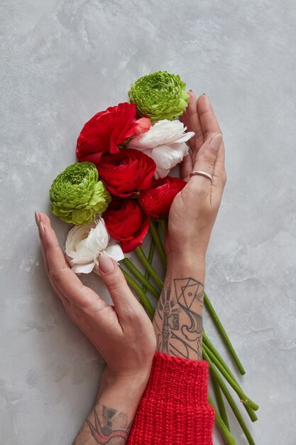 uma garota segurando um buquê de flores brancas, vermelhas e verdes sobre um fundo cinza de concreto. O conceito de um cartão de férias