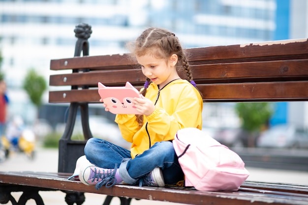 Uma garota segurando um tablet nas mãos Ela se senta do lado de fora em um banco As crianças usam tecnologia