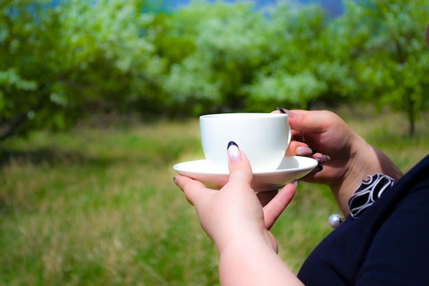 Uma garota segurando uma xícara de café na natureza em um parque florido