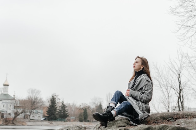 Uma garota senta em uma pedra em frente a um rio