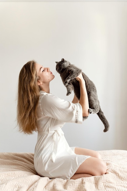 Uma garota sexy de pijama fino senta-se na cama e segura uma linda garota sexy de gato escocês em casa de pijama em uma cama com um animal de estimação
