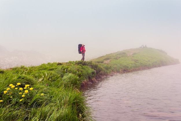 Uma garota solitária com uma mochila está de pé à beira do lago