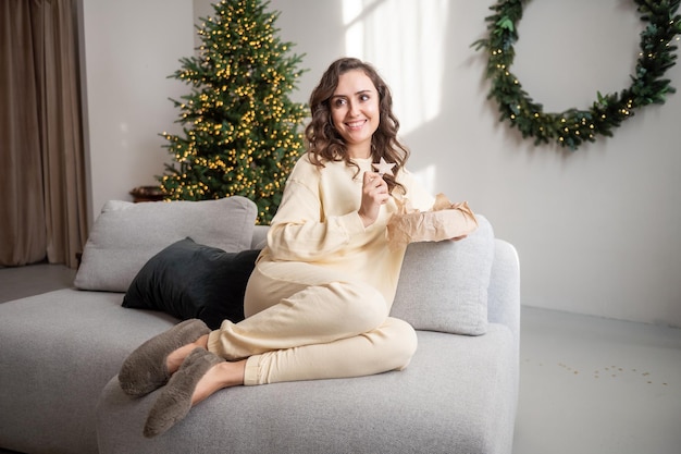 Uma garota sorridente com óculos está sentada em casa no sofá e segurando biscoitos de gengibre Desvia o olhar