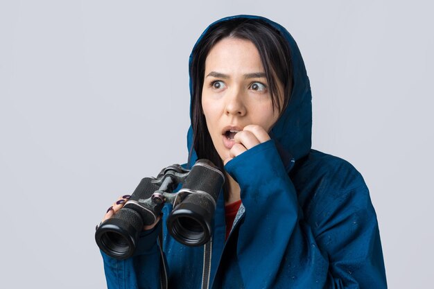 Uma garota turista com uma capa de chuva azul tem binóculos nas mãos e olha para longe, espiões.