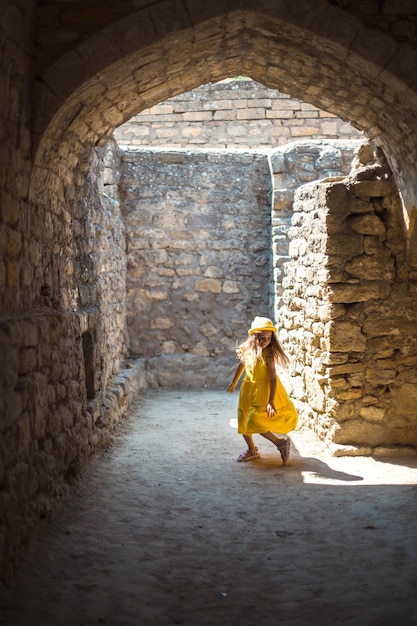 Uma garota turista de chapéu amarelo e vestido dançando ao longo da rua da cidade velha feita de pedra com um passeio turístico de fortaleza