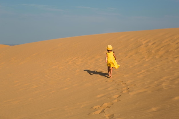 Uma garota turista de vestido amarelo corre ao longo de uma duna arenosa no deserto Vistas de viagem da duna Sarykum do Daguestão