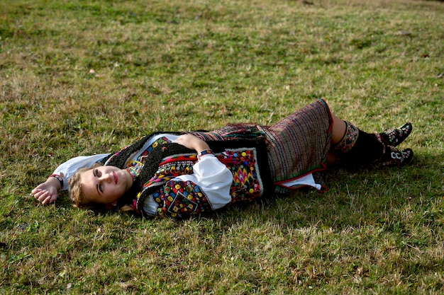 Uma garota ucraniana em um traje nacional Hutsul está deitada na grama em uma clareira na floresta