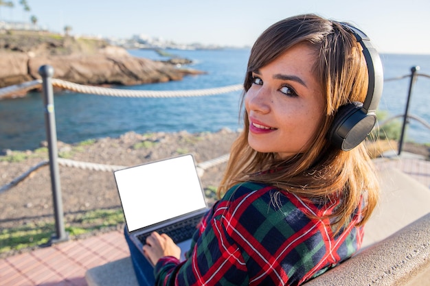 Uma garota usa seu laptop à beira-mar sentado em uma tela de banco com mock up