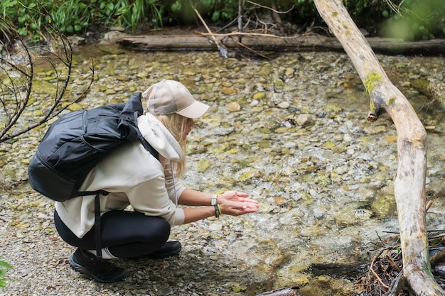 Uma garota viajante com uma pasta nas costas lava as mãos no rio no parque nacional