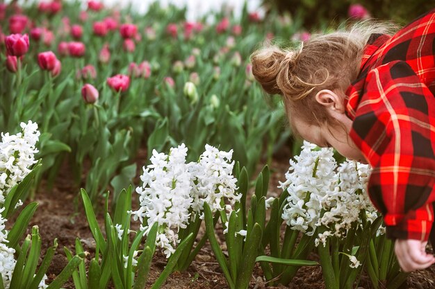 Uma garotinha admira flores em um canteiro bem cuidado da cidade e inala sua fragrância