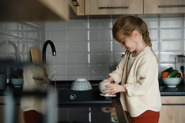 Uma garotinha ajuda a mãe a cozinhar e limpar na cozinha