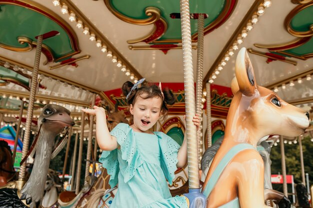 Uma garotinha alegre de vestido azul passeando em um parque de diversões