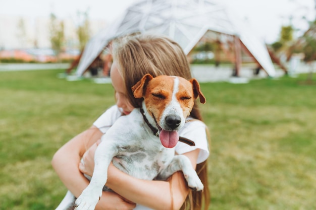 Uma garotinha beija e abraça seu cachorro jack russell terrier no parque amor entre o dono e o cachorro uma criança está segurando um cachorro nos braços