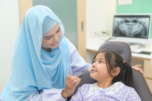 Uma garotinha bonita tendo os dentes examinados pelo dentista muçulmano nos dentes da clínica odontológica