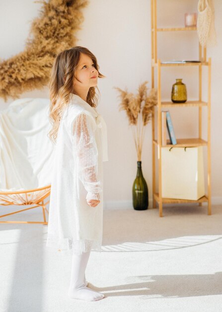 Uma garotinha bonitinha em um lindo vestido está dançando em uma sala ensolarada e brilhante A luz do sol cai da janela