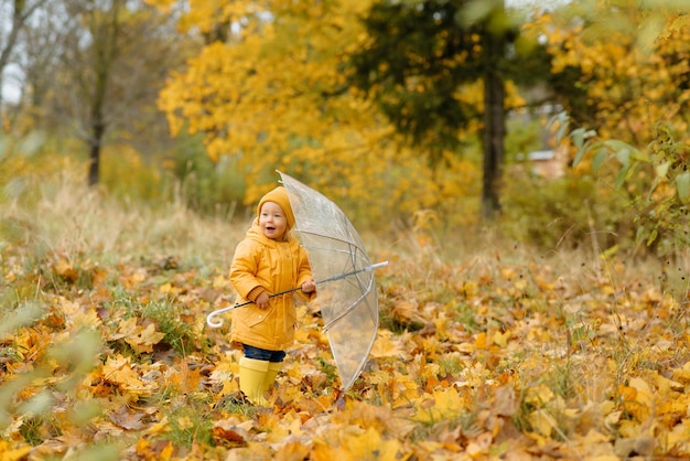 Uma garotinha caminha com um guarda-chuva em botas de borracha amarela e uma capa de chuva impermeável autumn walk