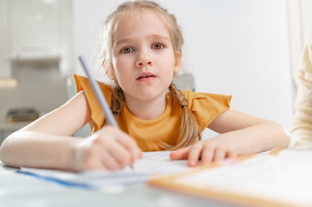 Uma garotinha cansada faz seu dever de casa. complexidades de uma caligrafia correta e bonita. não há desejo de aprender. família e ensino a distância