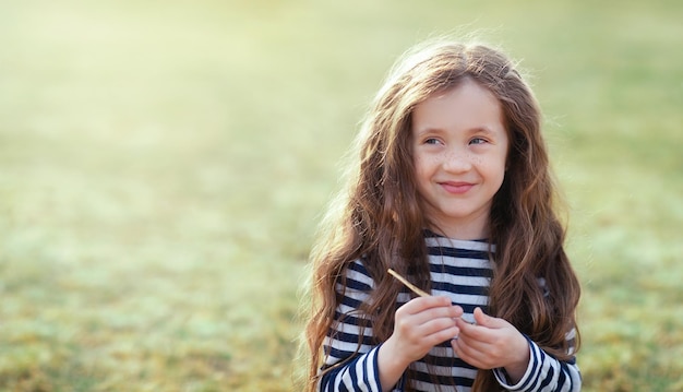 Uma garotinha com cabelo comprido e fofo está sorrindo para algo e olhando para longe