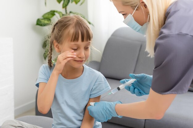 Uma garotinha com lágrimas nos olhos tem muito medo de vacinação. o bebê chora fechando os olhos de dor. retrato de uma criança soluçando que é injetada no ombro. conceito médico infantil,