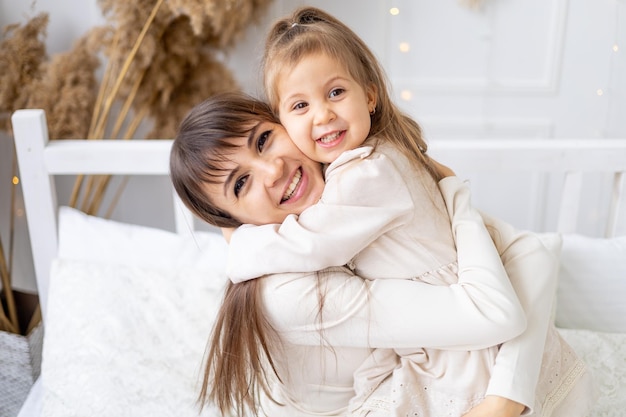 Uma garotinha com sua mãe abraçando e beijando em casa na cama Estilo de vida Família e maternidade felizes Dia Internacional da Mulher ou Dia das Mães Fotografia de alta qualidade