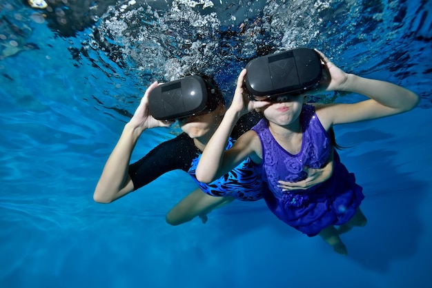 Uma garotinha com sua mãe em óculos pretos de realidade virtual na cabeça flutuando debaixo d'água