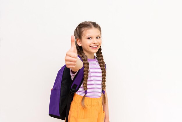 Uma garotinha com uma bolsa dá um polegar para cima uma linda criança está sorrindo em um fundo branco isolado