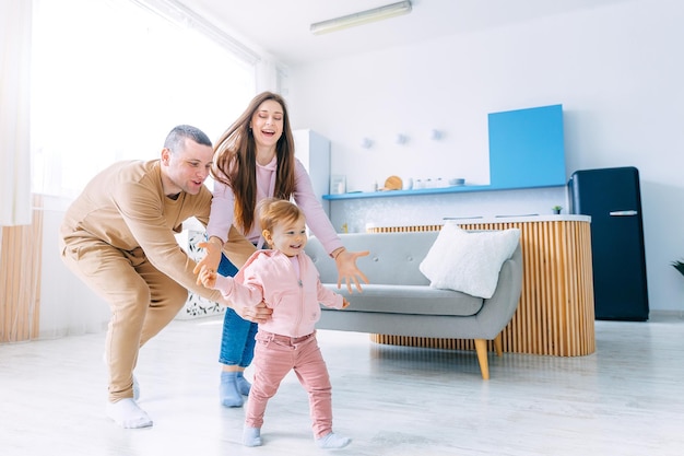 Uma garotinha corre pela sala feliz, os pais estão correndo atrás dela