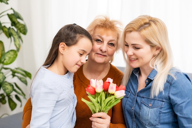 Uma garotinha dá um buquê de tulipas para sua mãe e avó. Eles comemoram o Dia das Mães. Eles têm um feriado familiar tradicional.