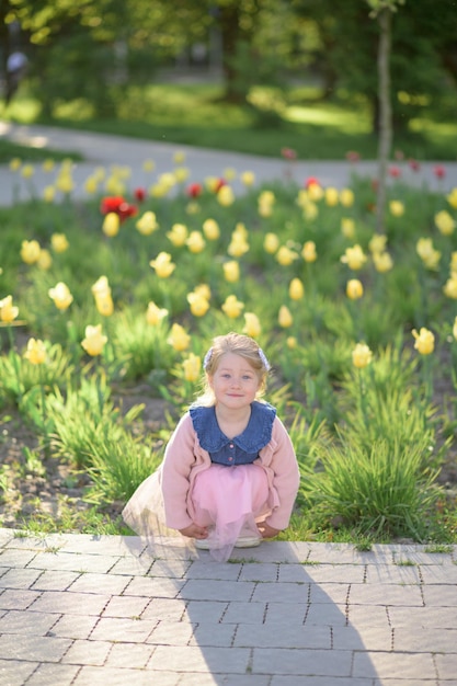 Uma garotinha de 3 anos caminha no parque com um vestido e um suéter rosa