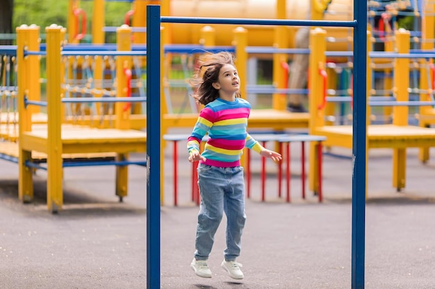 Uma garotinha de 56 anos em um jumper listrado brilhante pula no parquinho do parque