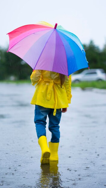 Uma garotinha de botas de borracha e eu com um guarda-chuva brilhante caminhamos por uma poça na chuva