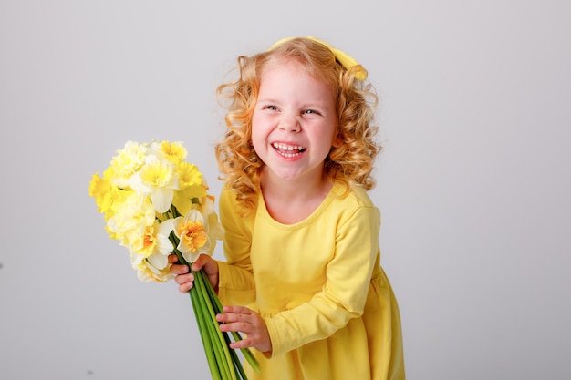 uma garotinha de cabelos encaracolados segura um buquê de flores de narciso amarelo da primavera em um fundo branco i