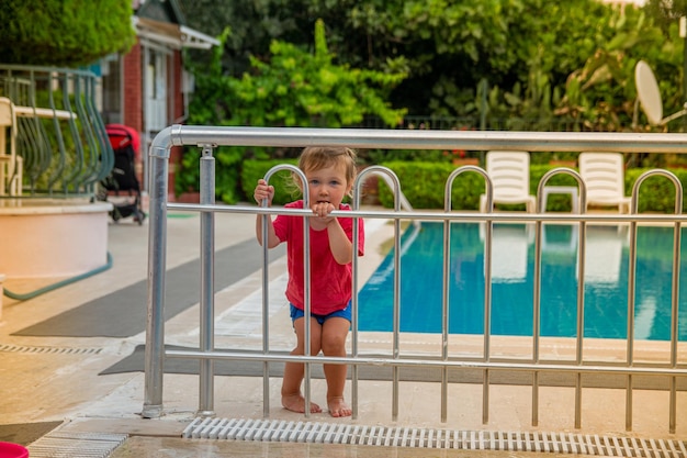 Uma garotinha de camiseta vermelha e short azul brinca com brinquedos perto da piscina