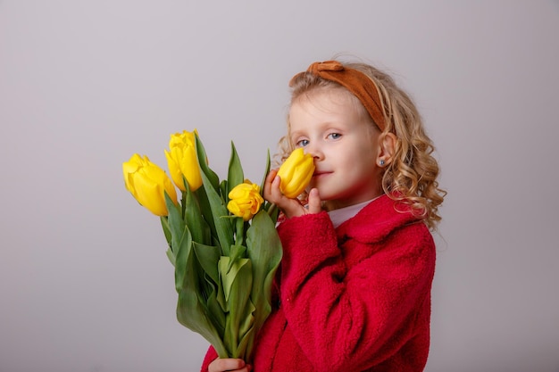 Uma garotinha de casaco vermelho segura um buquê de flores de tulipa da primavera em um fundo branco