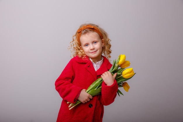 Uma garotinha de casaco vermelho segura um buquê de flores de tulipa da primavera em um fundo branco