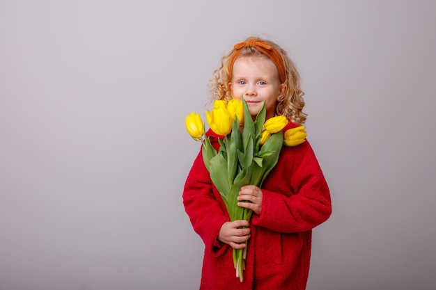 Uma garotinha de casaco vermelho segura um buquê de flores de tulipa da primavera em um fundo branco