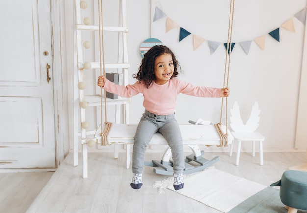 Uma garotinha de pele escura anda em um design de interiores de quarto infantil de balanço