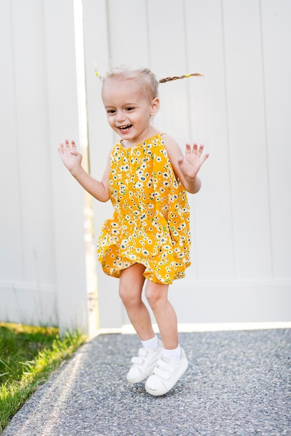 Foto uma garotinha de vestido amarelo está pulando na calçada.