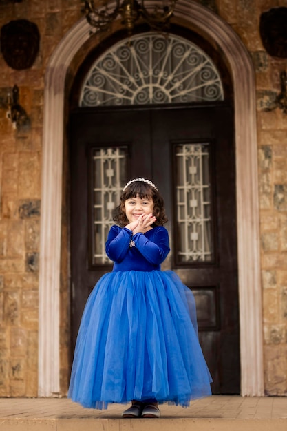 Uma garotinha de vestido azul marinho, parada na frente da porta da casa, e ela está feliz