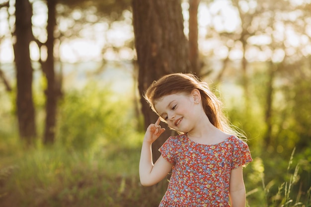 Uma garotinha de vestido branco e sandálias corre ao longo de uma estrada rural Ela tem um brinquedo nas mãos Feliz infância Férias de verão