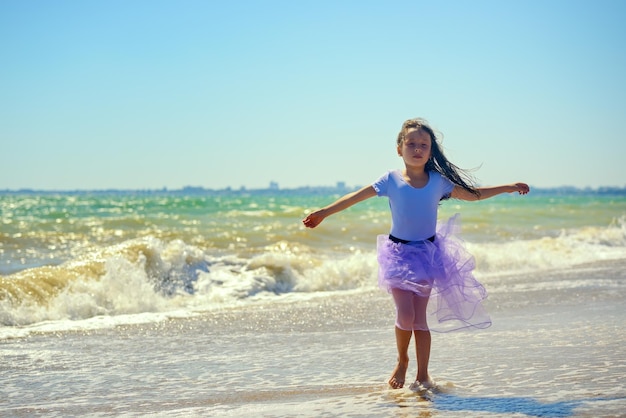 Uma garotinha de vestido roxo dançando na praia no contexto de ondas furiosas